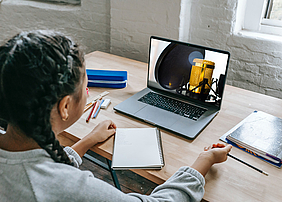 Symbolbild: Schülerin vor Laptop mit Mikrofon-Abbildung. Ursprüngliches Bildmaterial: Katerina Holmes, Jean Balzan (beide Pexels)
